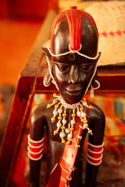 A wooden statue of a man with a mask on his face for sale in Kenya. The statue is brown and has a serious expression