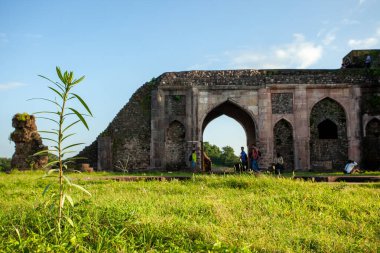 Gün batımını gören bir binanın kemerli kapısı. Manzara ağaçlı bir tepe, Mandu, Hindistan.
