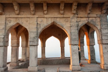 The arched doorway of a building with a view of the sunset. The view is of a hill with trees, Mandu, India. clipart