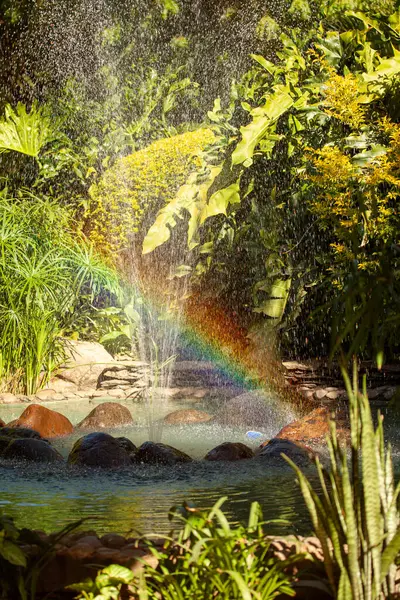 A water fountain with a rainbow in the air. The water is clear and the rainbow is bright. The scene is peaceful and serene