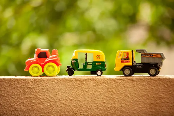 Three toy vehicles are lined up on a wall, with a truck on the right and a car and a tuk-tuk on the left