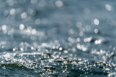 Yüzeyde dalgalanmaları olan mavi su bulanık mavi renkli berrak, durgun su yüzeyi dokusu sıçrama ve kabarcıklarla aydınlık desenli su dalgaları.