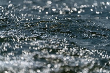 Yüzeyde dalgalanmaları olan mavi su bulanık mavi renkli berrak, durgun su yüzeyi dokusu sıçrama ve kabarcıklarla aydınlık desenli su dalgaları.