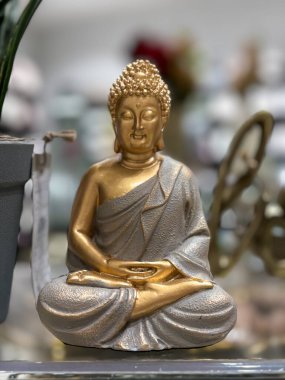 Lotus pozisyonunda oturan bir Buda 'nın altın ve gümüş heykeli. Heykel bir rafta duruyor ve etrafı başka eşyalarla çevrili.