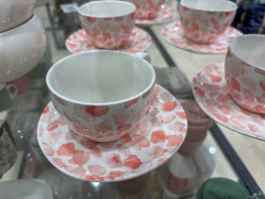 Cam bir rafta pembe, beyaz fincanlar ve tabaklar sergileniyor.