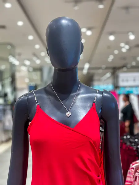 A mannequin wearing a red dress and a heart necklace. The mannequin is standing in a store