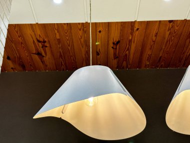 Tavandan sarkan üç beyaz lamba, biri şapka şeklinde. Odanın modern ve minimalist bir tasarımı var.