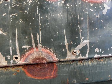 Delikleri ve boya lekeleri olan paslı metal bir yüzey. Yüzey eski ve yıpranmış görünüyor. Çürüme ve terk edilme hissi var.