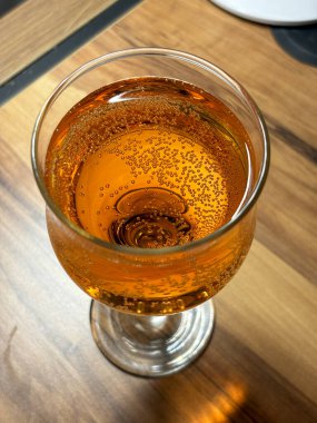 Tahta bir masanın üzerinde bir bardak şarap duruyor. Şarap uzun, ince bir bardakta, saplı. Şarap koyu kırmızı renktedir ve içinde kabarcıklar vardır..