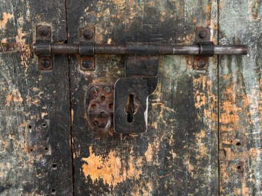 A rusty metal handle is shown on a wooden surface. The handle is old and worn, with a few holes in it. The image has a vintage feel to it, and the rusty metal handle gives it a sense of age