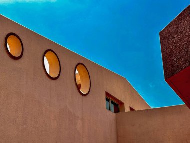 Binanın arka planında mavi gökyüzü olan üç penceresi var. Pencereler dairesel ve bina kahverengi.