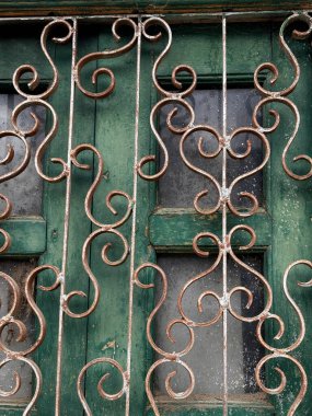 Demir parmaklıkları ve cam camı olan yeşil bir pencere. Pencere, taş duvarlı bir binanın üzerinde.