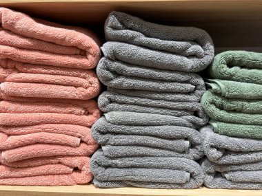 Biri pembe, biri gri ve biri yeşil olan bir yığın havlu. Havlular üst üste dizilmiş raflarda.