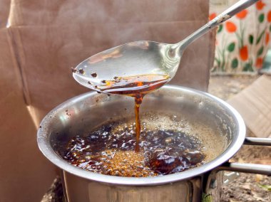 Bir kaşık, tencereden kalın kahverengi bir sıvı topluyor. Sıvı bir sos ya da sos gibi görünüyor ve bir kaseye dökülüyor. Yemek pişirme ya da yemek hazırlama kavramı