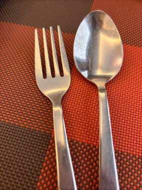 Bir çatal ve kaşık kareli bir masa örtüsünün üzerindedir. Çatal bükülmüş ve kaşık parlak.