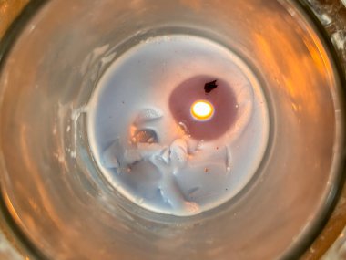 Cam bir kavanozda bir mum yakılır. Kavanozun yarısı erimiş balmumuyla dolu. Odadaki tek ışık mum.