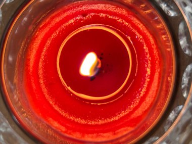 Cam bir kavanozda kırmızı bir mum yakılır. Mum yanıyor ve alevler görünüyor.