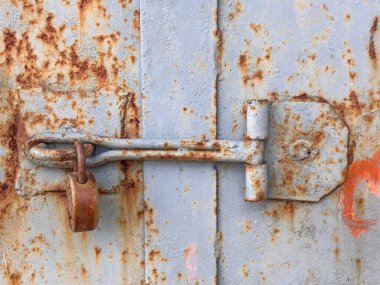 Paslı bir kilit metal bir kapıya bağlıdır. Kilit paslanmış ve kapı da eski.
