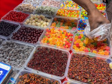 Bir insan bir yığın şekerin içine uzanıyor. Şekerler çok farklı renkte ve şekillerde.