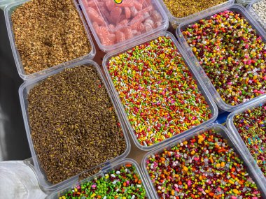 Açık plastik kaplarda çeşitli renkli şeker ve baharatlar sergilenir. Şekerler sıra sıra dizilmiş, bazı kaplar diğerlerinden daha renkli şekerler içeriyor.