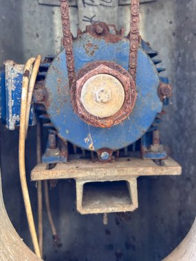 Üzerinde zincir olan paslı eski bir motor. Motor mavi ve üzerinde beyaz etiket var.