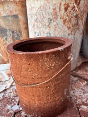 Tutacağı olan paslı bir kova tuğla duvarda durur. Kova boş ve yıpranmış görünüyor.