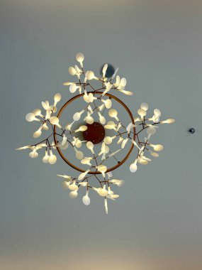 Üzerinde bir sürü küçük ışık olan büyük bir aydınlatma armatürü. Ampul tavandan sarkıyor ve yanıyor.