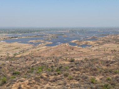 Birkaç ağaç ve birkaç güneş paneli olan bir çöl manzarası. Gökyüzü açık ve güneş parlıyor.