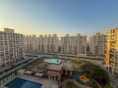 Havuzu ve oyun alanı olan büyük bir apartman manzarası. Gökyüzü mavi ve güneş batıyor.