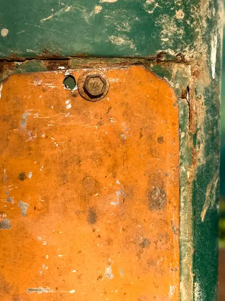 Üzerinde yeşil ve turuncu etiket olan paslı bir metal direk. Etikette bir cıvata eksik.