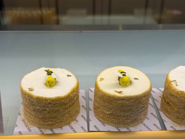 Tezgahta üzerinde arı olan üç kek sergileniyor. Pastalar sarı ve beyaz kremayla süslenir ve altın rengi kahverengidir. Pastalar sıraya dizildi.