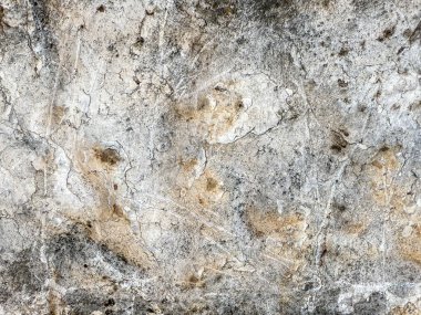 Üzerinde bir sürü çatlak ve kir olan bir duvar. Duvar taştan yapılmış ve pürüzlü bir dokusu var.