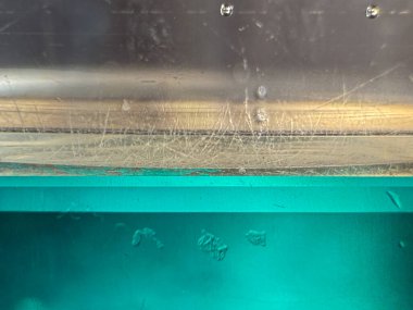 Üzerinde yeşilimsi bir renk ve birkaç çizik olan berrak bir bardak. Çizikler camın tam ortasında ve farklı boyutlarda.