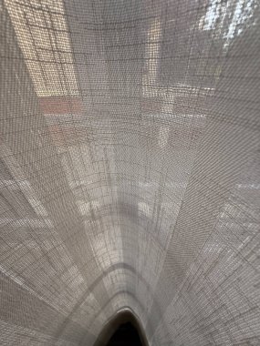 Çizgi ve noktalardan oluşan beyaz bir kumaş. Kumaş pencereden sarkıyor. Pencereden gelen ışık kumaşın üzerine gölge düşürüyor.