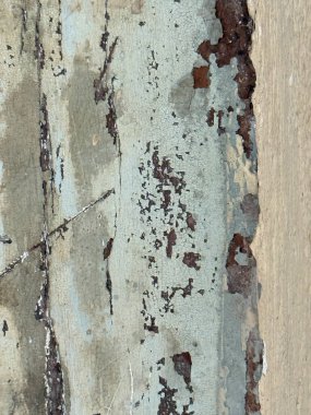 Duvar kabuk soyma boyasıyla kaplı ve pürüzlü bir dokusu var. Mavi boya soluyor ve duvar eski ve yıpranmış görünüyor.