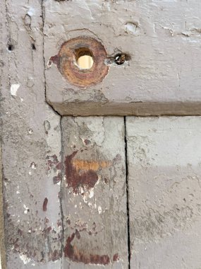 İçinde delik olan ahşap bir kapı. Çukur paslı ve içinde vida var. Kapı eski ve yıpranmış.