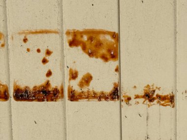 Üzerinde kahverengi lekeler olan bir duvar. Lekeler kare şeklinde ve tüm duvara yayılmış vaziyette. Duvar eski ve yıpranmış görünüyor. Lekeler eski görünümüne ekleniyor.