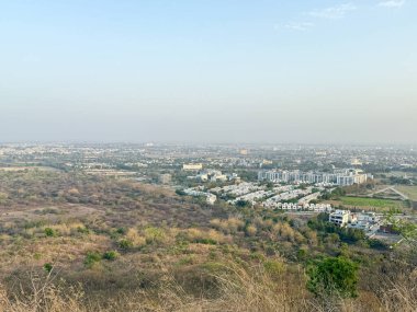 Bir sürü bina ve birkaç ağacın olduğu bir şehir manzarası. Gökyüzü açık ve güneş parlıyor.
