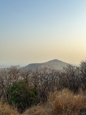 Arka planda bulutlu bir gökyüzü olan bir dağ sırası. Gökyüzü mavi ve gri karışımı. Sahneye sakin ve huzurlu bir atmosfer veriyor.