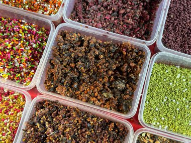 Plastik kaplarda çeşitli baharat ve bitkiler sergilenir. Baharatlar kırmızı ve yeşil baharatlar içeren bazı kaplar ile renkli ve görsel olarak çekici bir şekilde düzenlenmiştir.