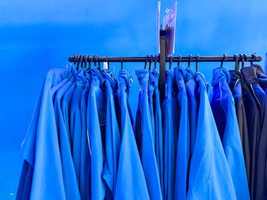 Mavi bir duvarda asılı mavi bir ceket askısı. Ceketlerin hepsi aynı renk ve sırayla asılılar.