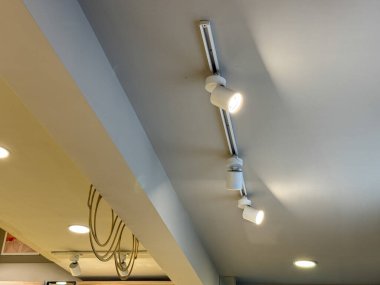 Tavandan beyaz bir ışık armatürü sarkıyor. Alet üç lambadan oluşuyor. Her biri farklı bir yöne bakıyor.