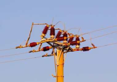 Kırsal kesimin arka planında elektrik kabloları ve elektrik direkleri var. Yüksek voltajlı elektrik iletiminin retro aygıtı mavi gökyüzünün arka planında bir kabloyla.