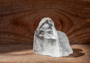 Bir beyaz, berrak taş kristal. Tahta zemin ve arka planda yansımaları olan yarı değerli iyileştirici kristal. Güneşli, güneşli.