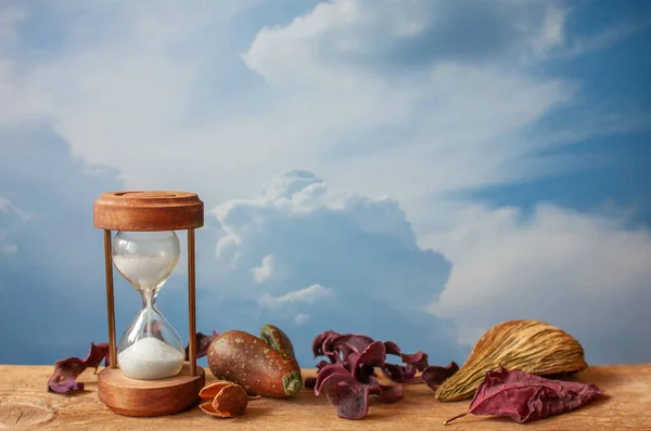Still life with old vintage clock, retro style. Vintage clock, hourglass on wooden board with dry natural decoration, blank sky background for possible text.