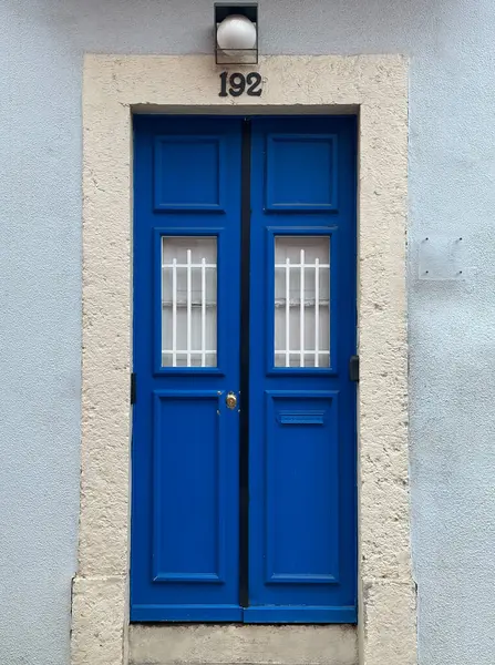 Canlı, mavi, bej taşla çerçevelenmiş, kafa kafaya çekilmiş bir çift kapı. 192 numara kapının üstünde görünüyor.. 