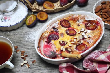 Damson mavisi erik pudingi (turta) ve bir fincan çay, krema şekeri ve badem sosu, ahşap zemin üzerinde Fransız mutfağı. Kırsal biçim