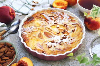 Bademli nektarin clafoutis (turta), kremalı şeker sosu ve bir fincan çay, açık arkaplanda Fransız mutfağı