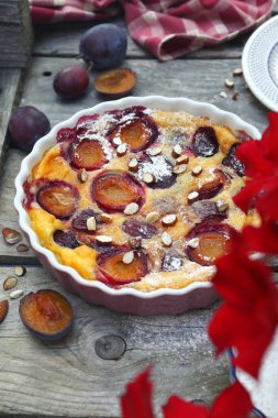 Damson Blue Pum Clafoutis (turta), krema şekeri ve badem sosu, ahşap arka planda Fransız mutfağı. Kırsal tarzda. Üst görünüm
