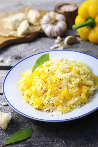 Italian food. Plate of yellow bell pepper risotto and grated parmesan cheese on wooden background